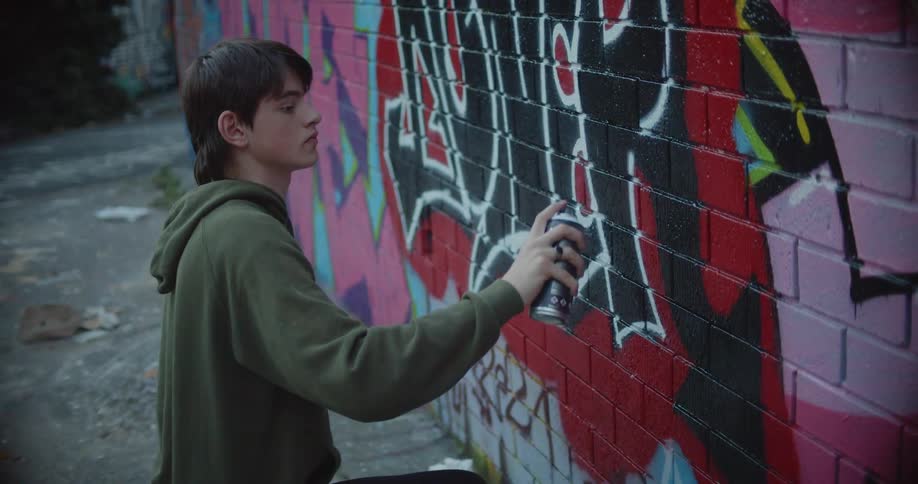 A teenager is spraying graffiti on the brick wall