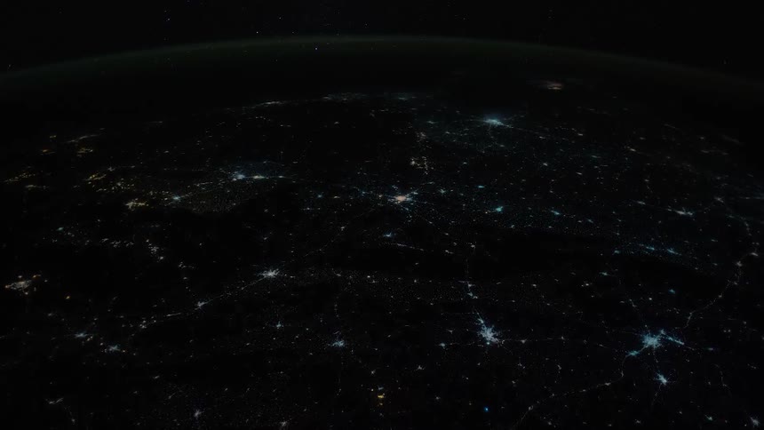 Clusters of urban lights contrast withdarkness at night ending in complete black with lighting over ocean