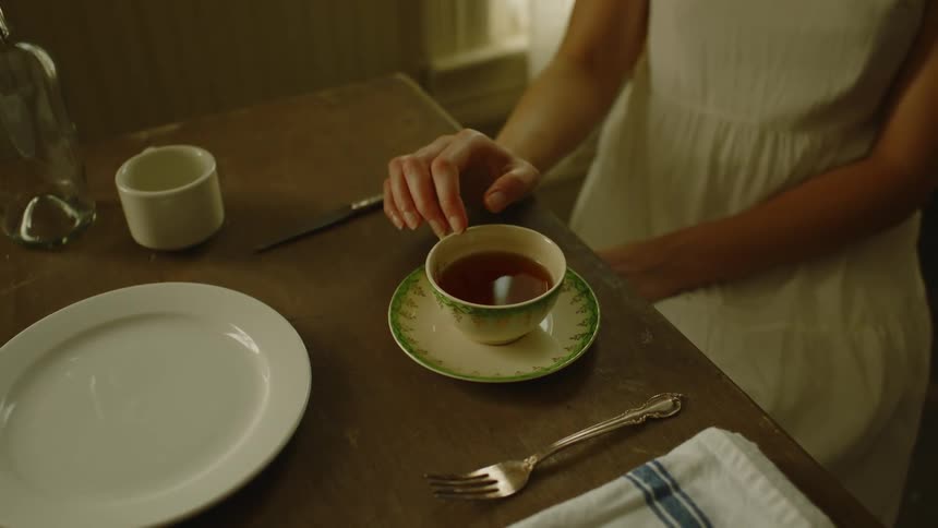 Woman sitting in front of a cup of tea on the kitchen table at home