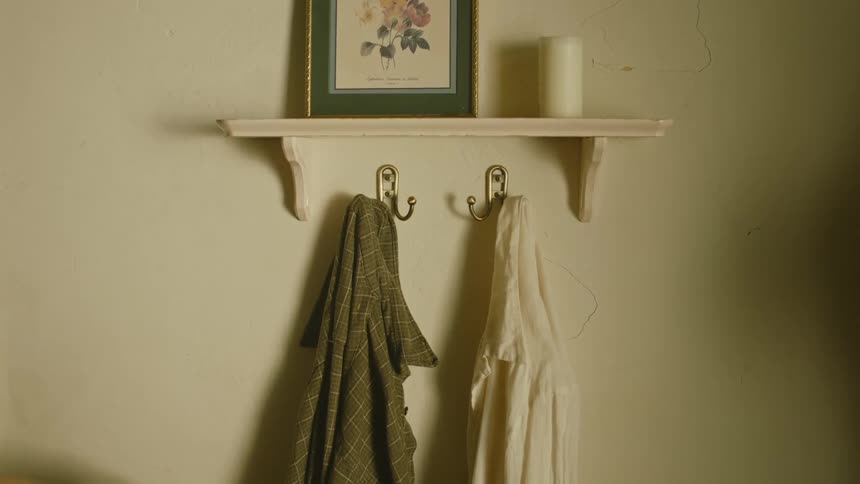 A woman rests her hand on a shirt hanging on a wall hanger for a moment before slowly walking away