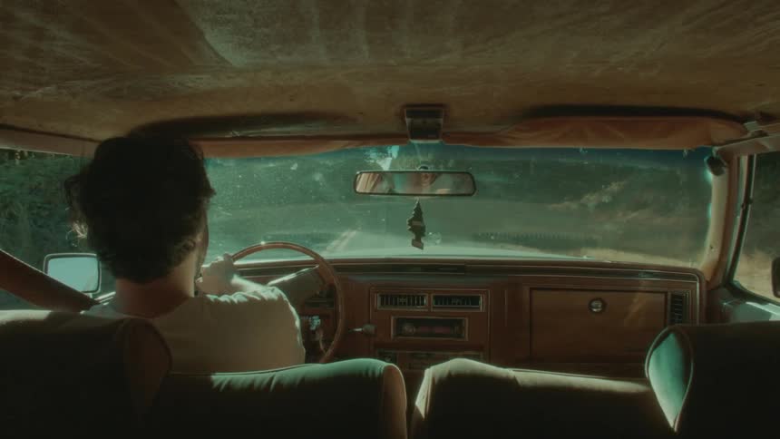 A man driving a vintage car turns onto a tree lined road