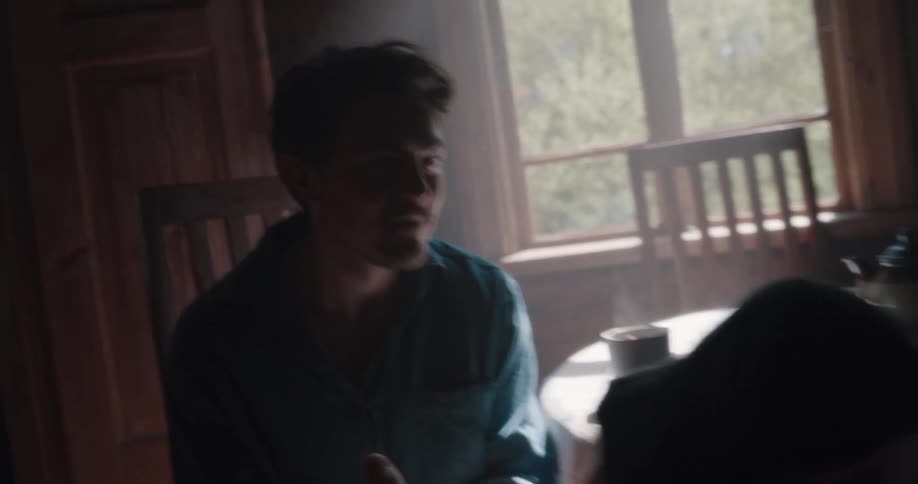 Man teases woman as they sit in dining room by pretending to bite her toes