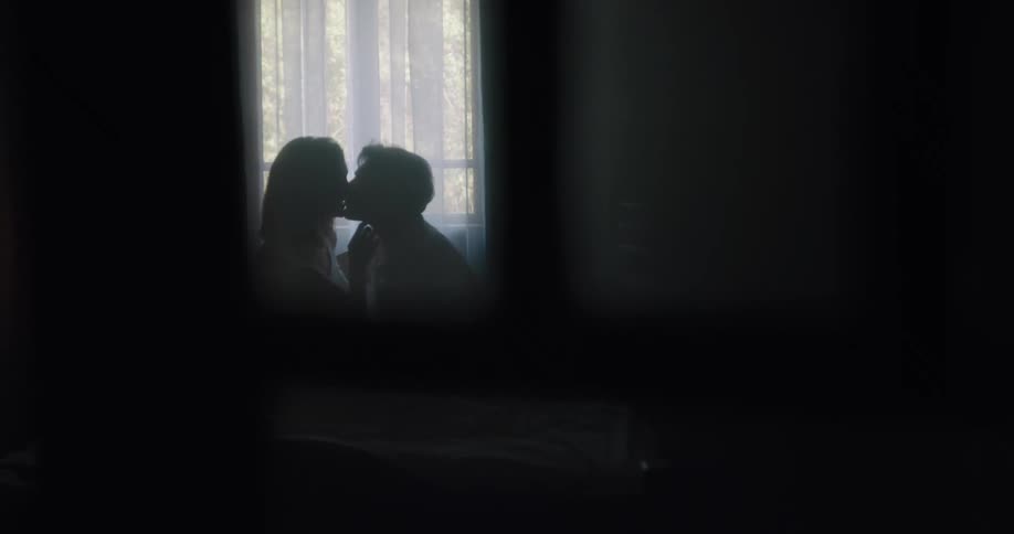 Silhouette of a young couple kissing on the bed inside a dimly lit room