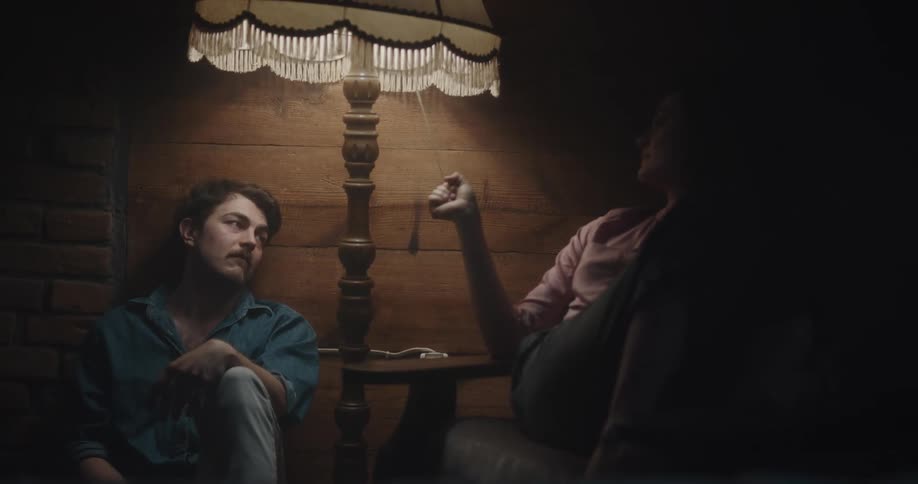 A man and a woman sitting in a room with the woman turning on and off a lamp with a wall in the background