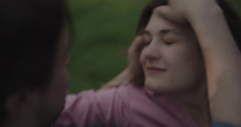 A man and a woman hugging and kissing with grass in the background