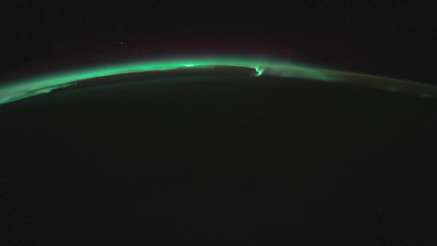 The green lights of the aurora curve around the earths surface against the black of space