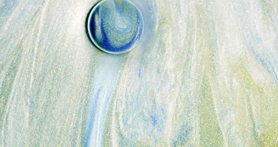 A liquid comprised of many colors as well as glitter flows around a large droplet that is rolling along its surface