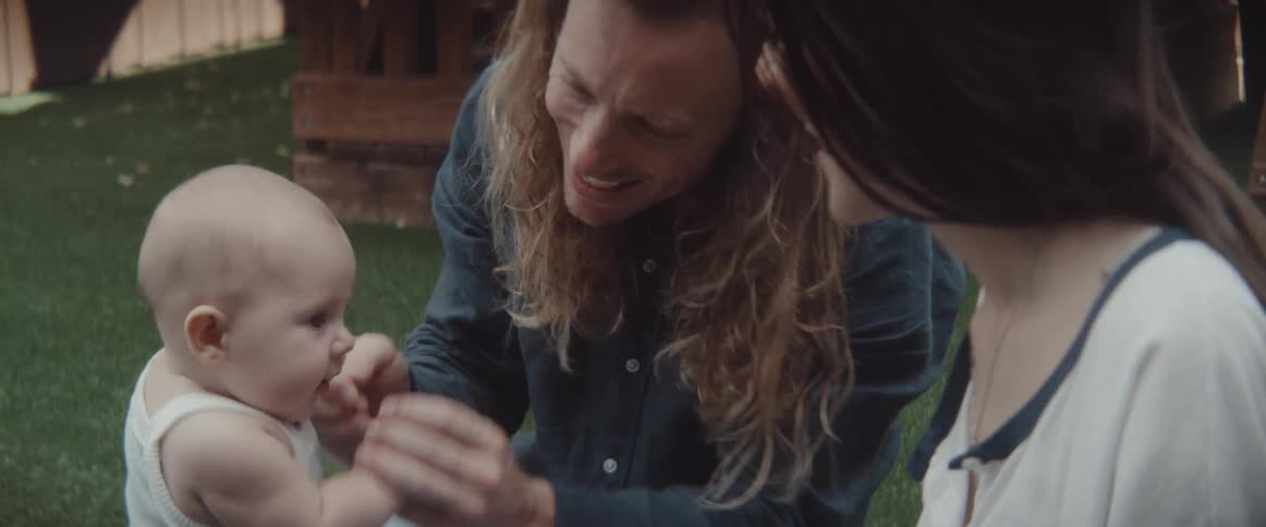 A man and woman sit on the grass and play with an infant