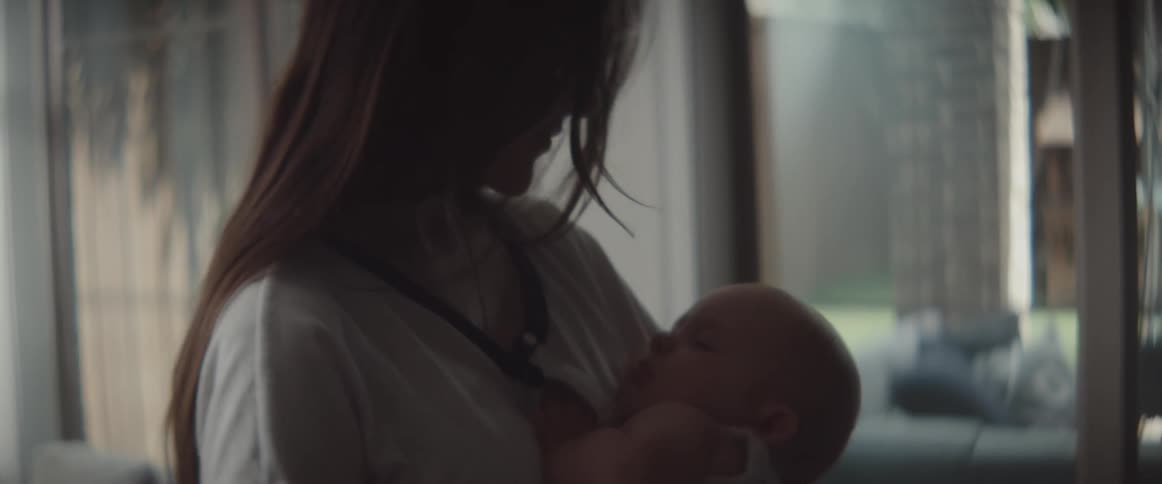 Brunette mother with long hair holds baby to make him sleep in the living room at home