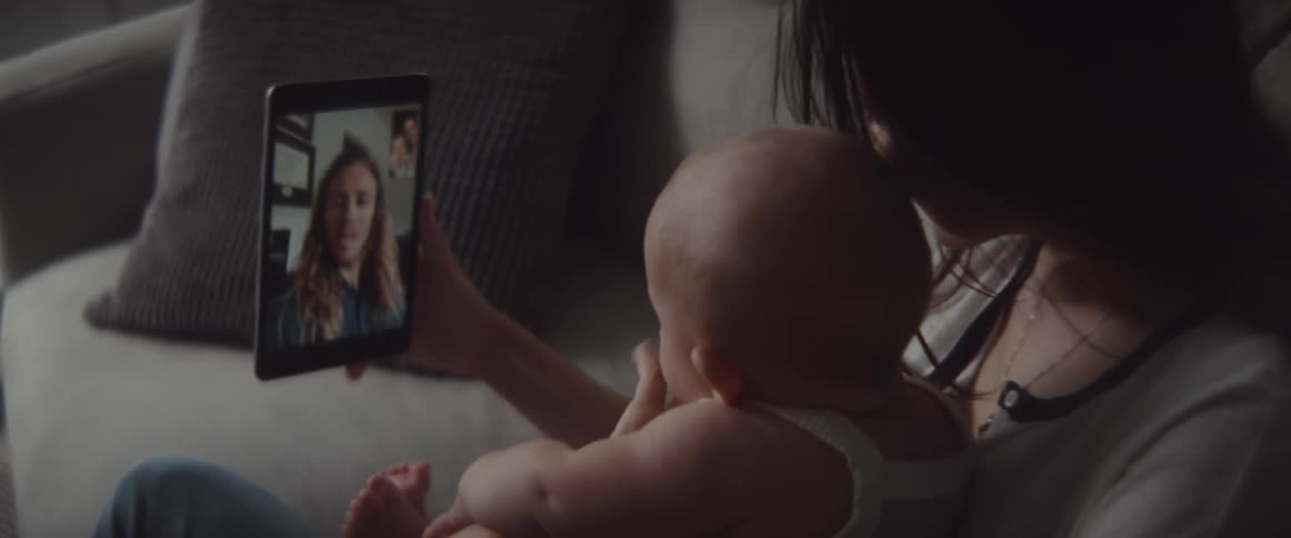 A woman in a room sitting on a couch holding a baby and a tablet
