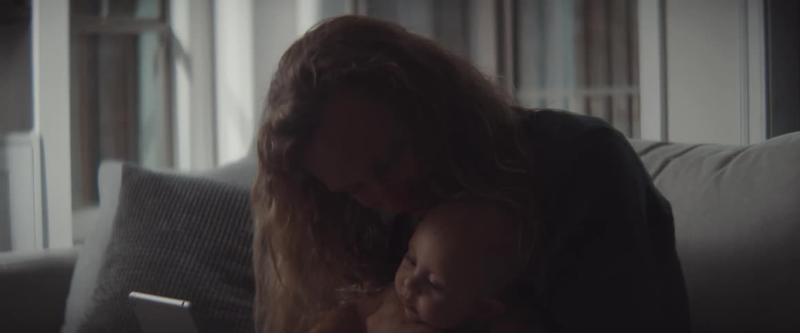 A man sits on a couch and kisses his baby son as he looks at a tablet