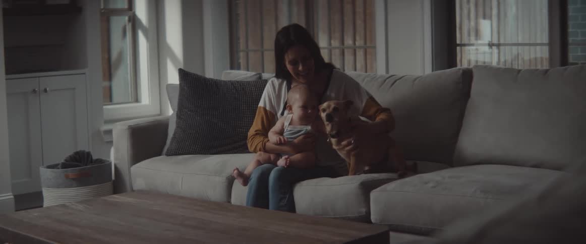 A woman sitting at home on a couch calls her dog up