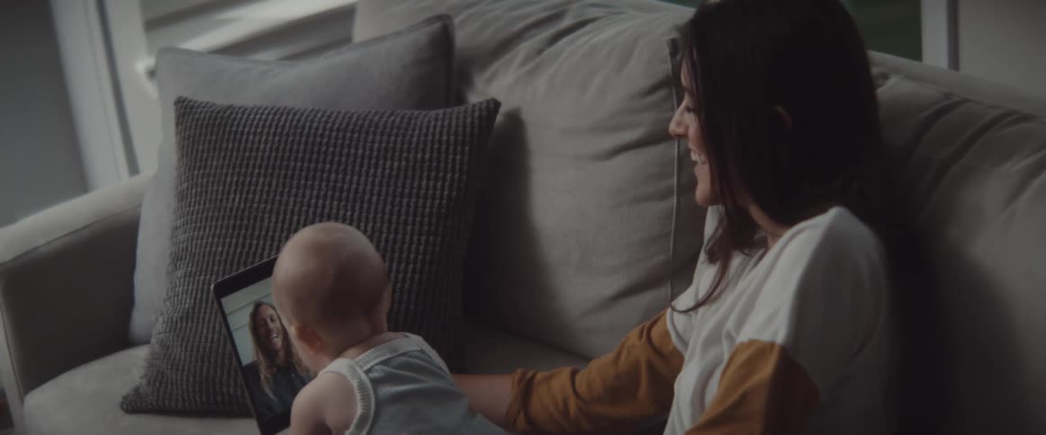A woman in a room sitting on a couch holding a baby and a tablet