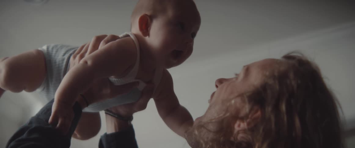A man playfully lifts a baby above his head in a house during the day