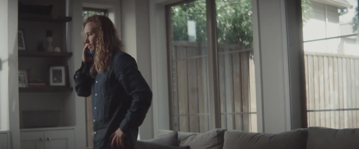 A man gets up from his couch and paces while talking on the phone