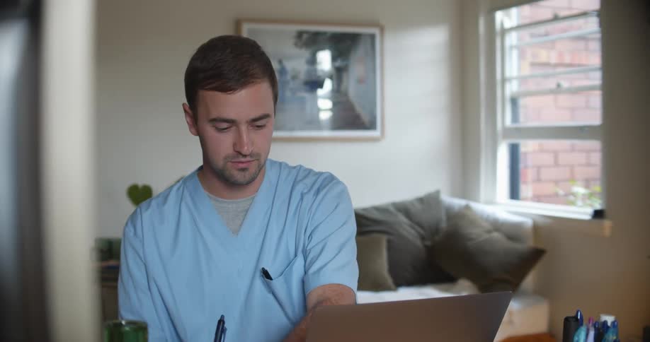 Young male nurse working from home in front of a laptop