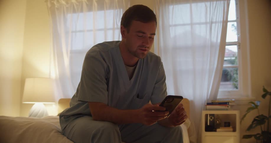 A man is talking on his cell phone while sitting in bed