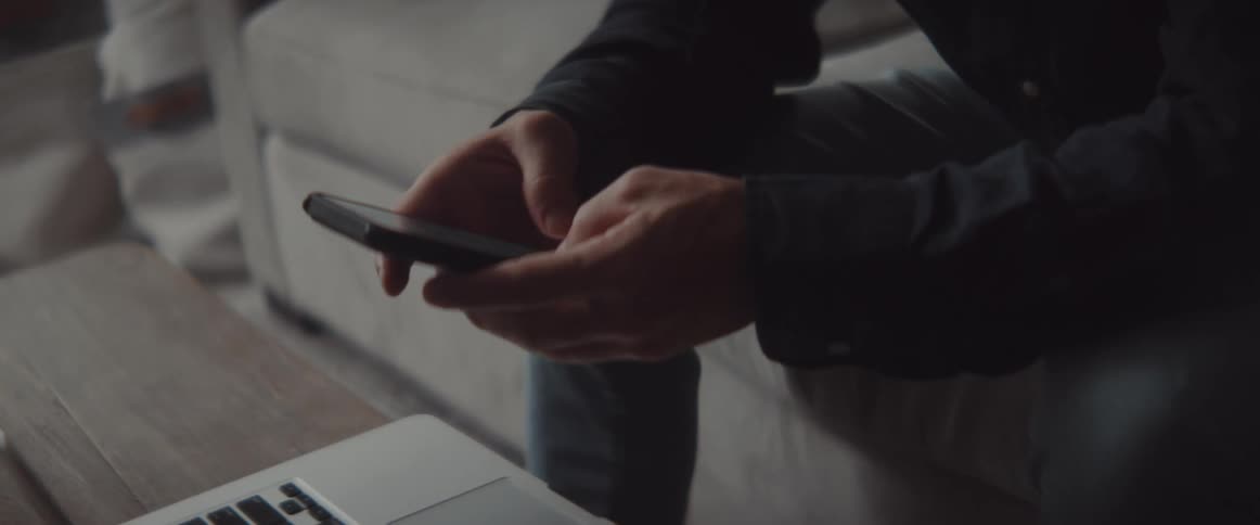 A person working on a laptop starts texting on a smartphone at home