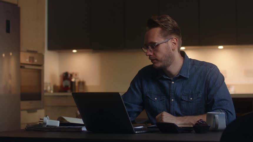 A man picks up a pen to make a note before going back to his laptop
