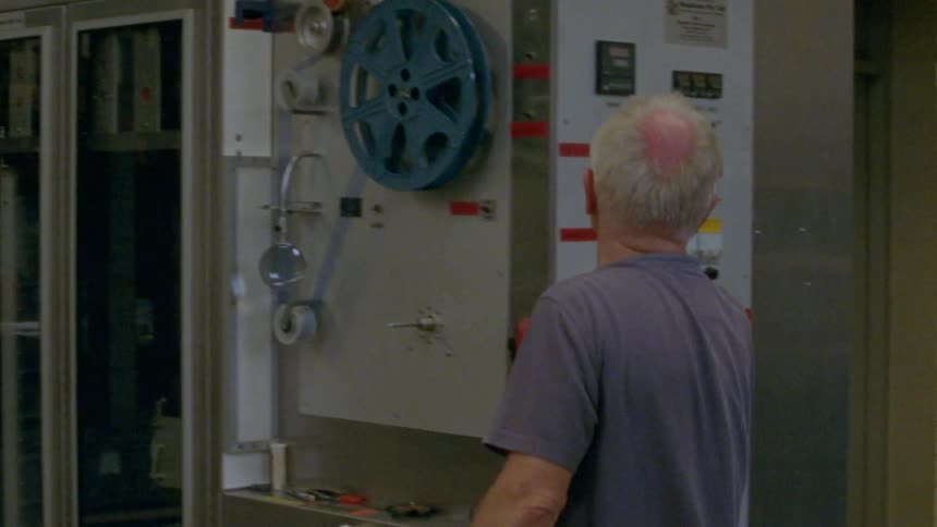 A man with glasses in a factory turning off lights and touching switches on a machine
