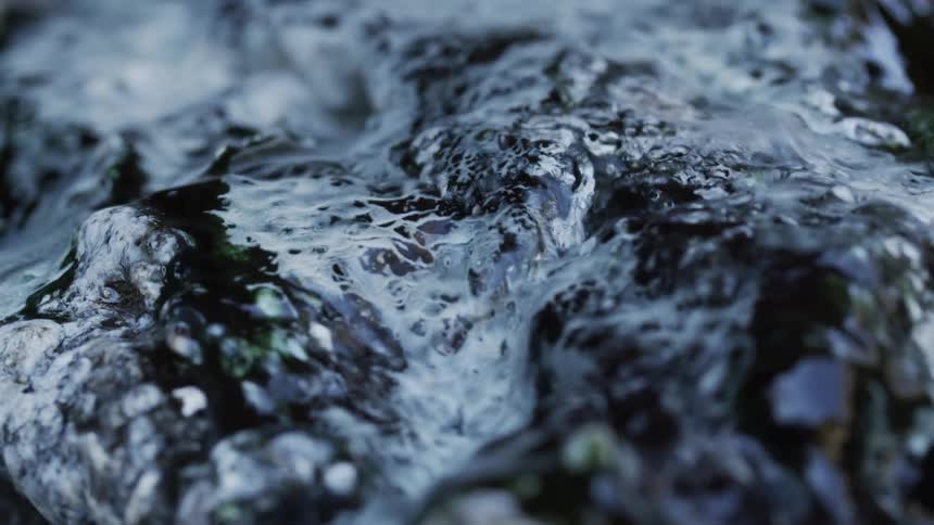 Water flows down craggy gray and black rock with green and gold inclusions