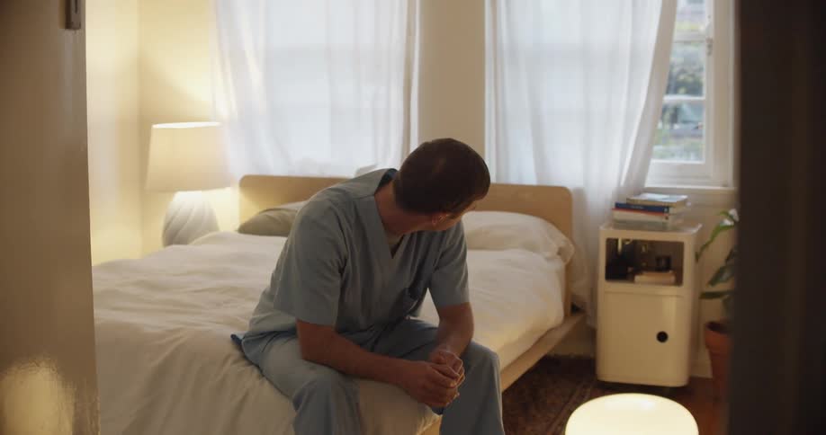 A man is sitting on the bed holding his hands together