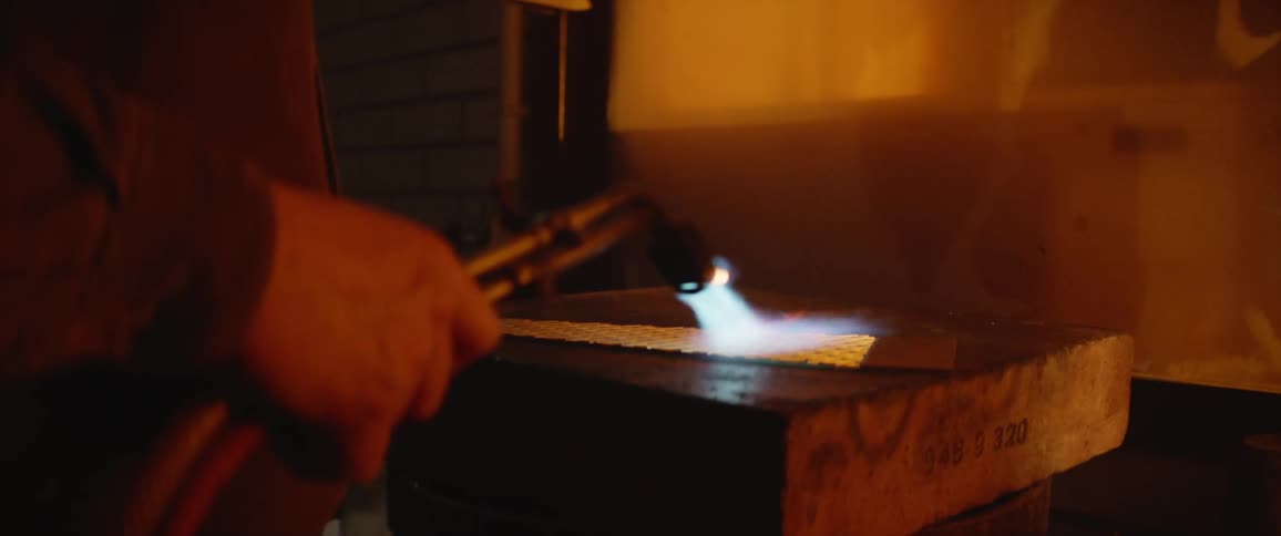 A person in a room using a blowtorch with fire on a piece of metal