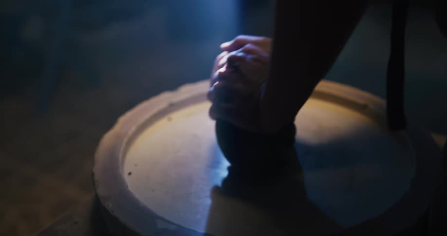 A person kneading clay for pottery over a table inside a dimly lit shop