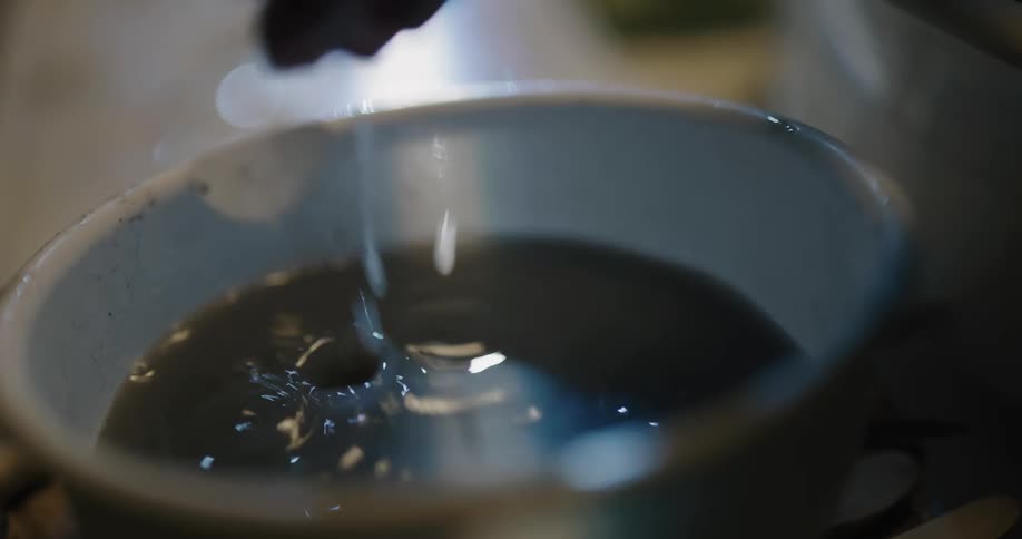 Person rinses hands in liquid reflecting light that is contained in chipped white bowl