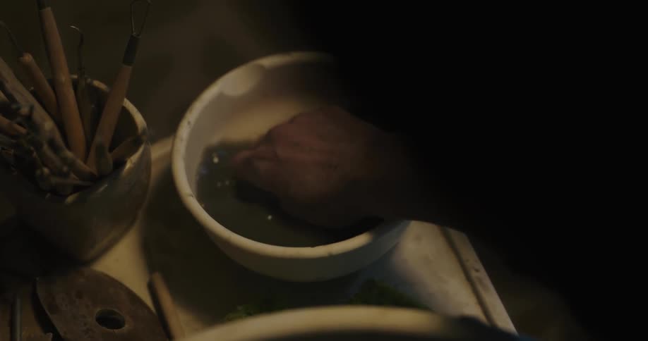 Person working at pottery wheel dips hand it liquid