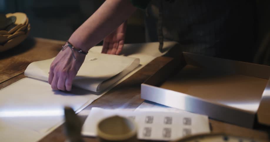 A person in a room putting a sticker on wrapping paper and placing it inside a box