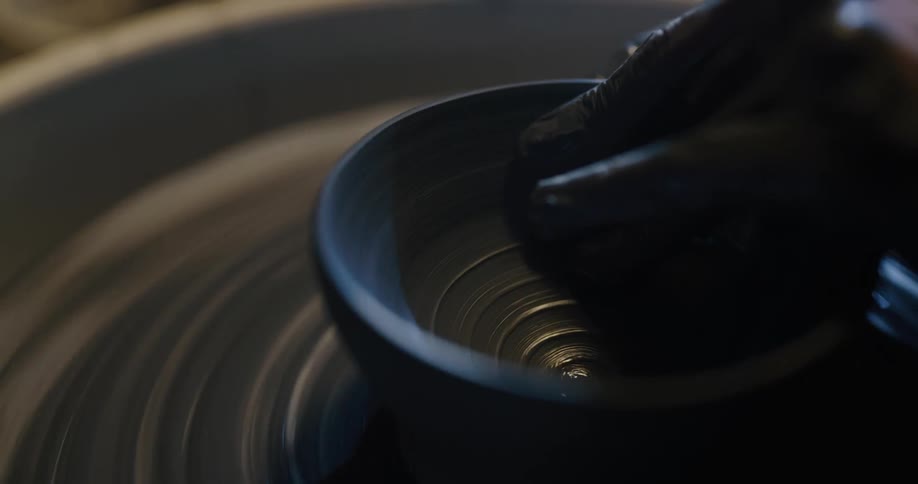 A potter holds onto the top of a potters wheel as it spins around and around