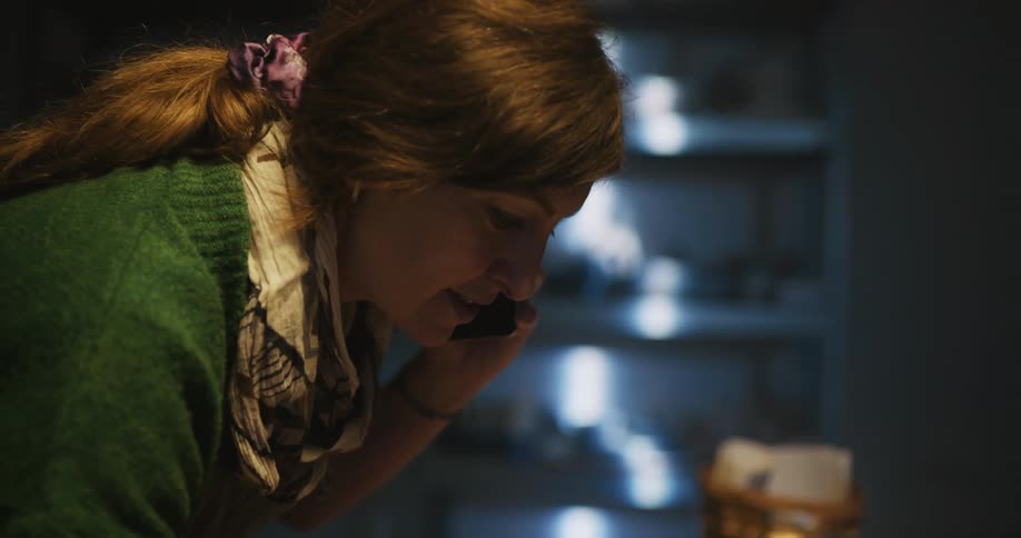 A woman talks on the phone as she leans over a counter working on a laptop
