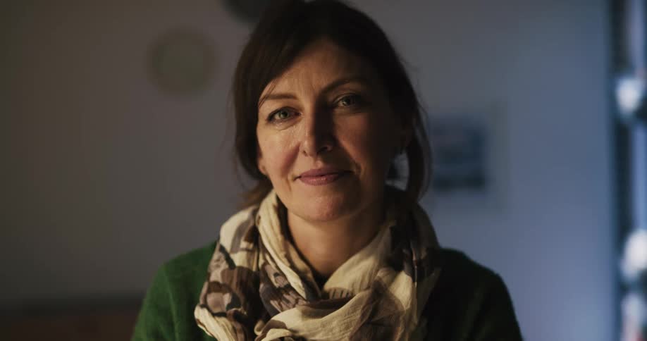 A woman turns her head to gaze into the camera before smiling