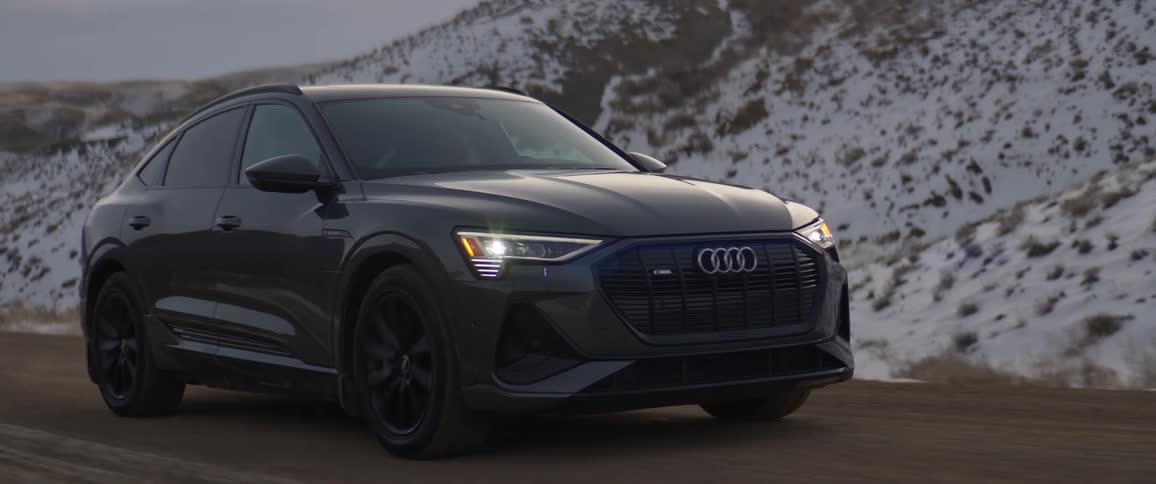 Audi car drives on road next to snowy hills