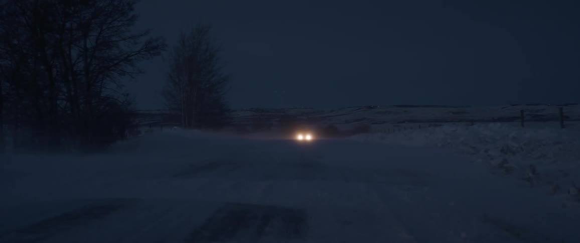 A car drives through a snowy rural area