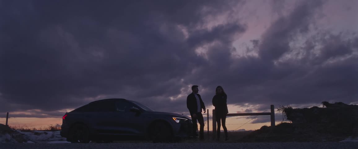 Young couple talking on a road in the countryside near a parked car at sunset