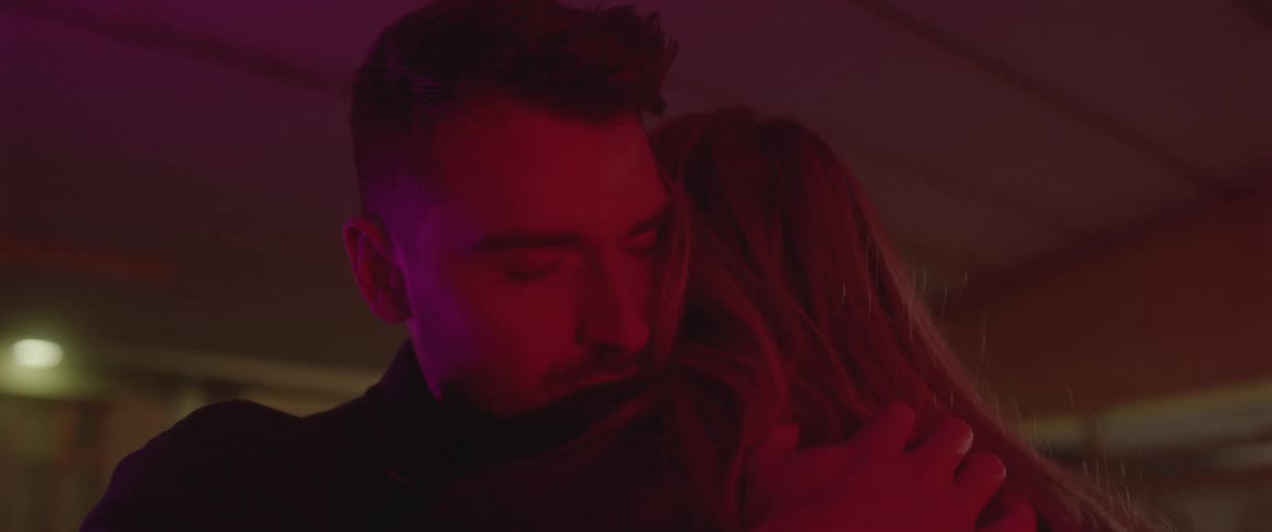 Man with a stubble beard and blonde woman embrace one another warmly