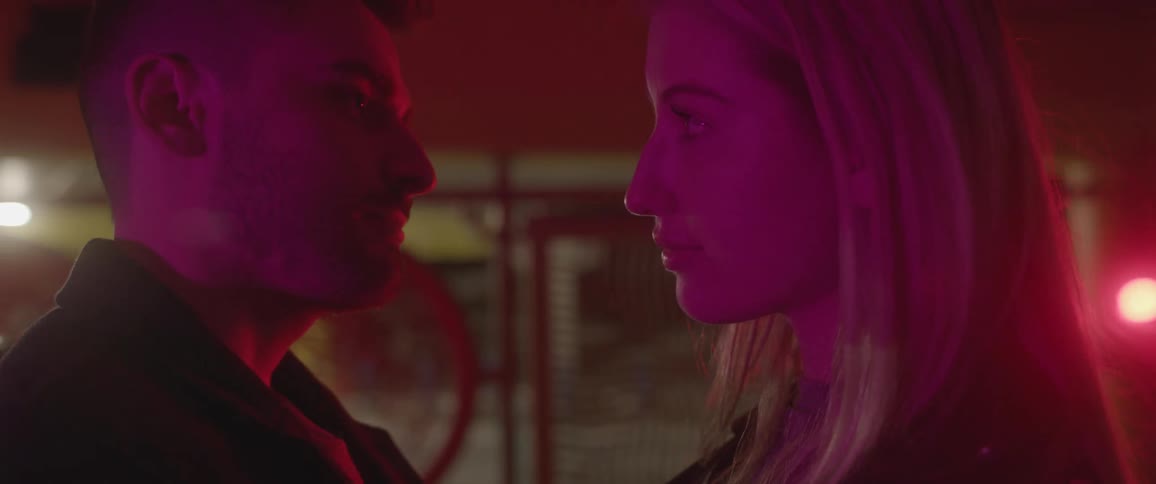 Couple stands close together under purple lights before hugging