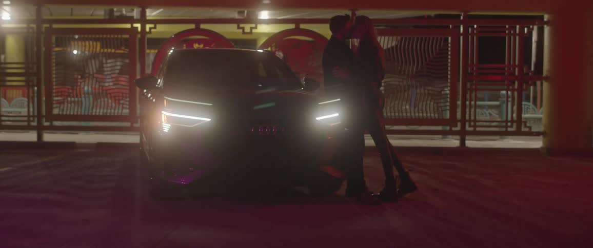 A man and woman kissing against a car