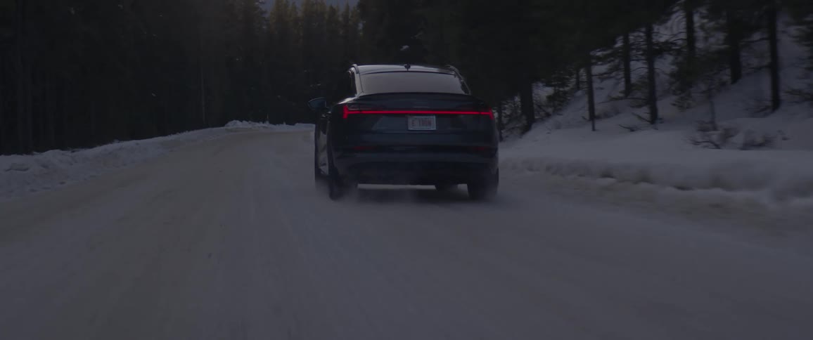 A vehicle travels along a snowy road through a forest during the day