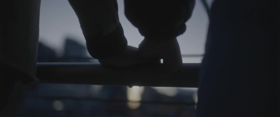 Couple holding hands on a bridge near the city skyline at sunset