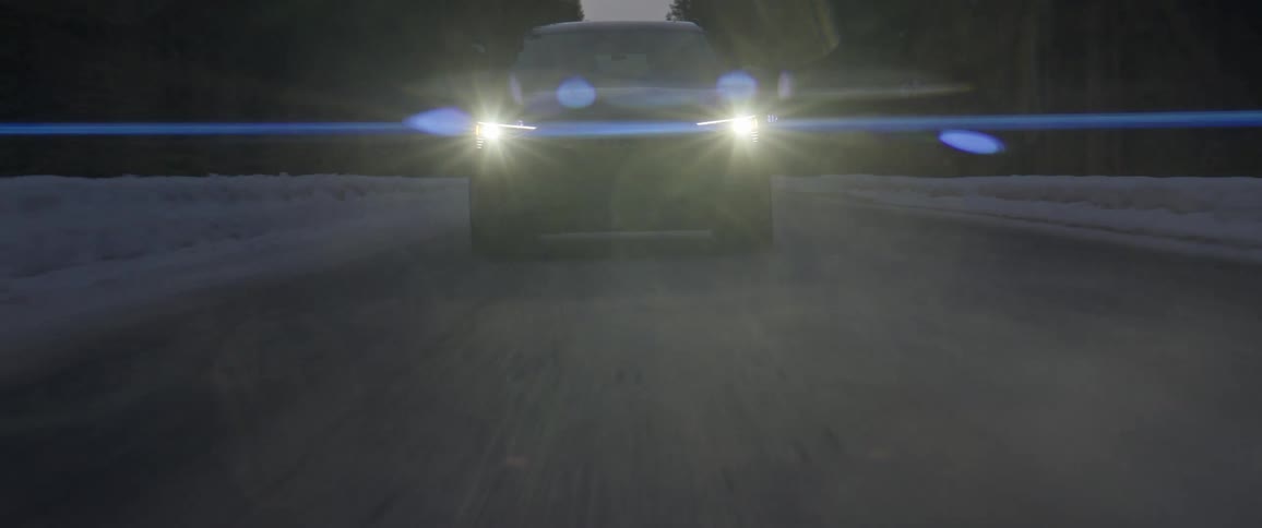 A vehicle driving on a snowy road with trees the sky and clouds in the background