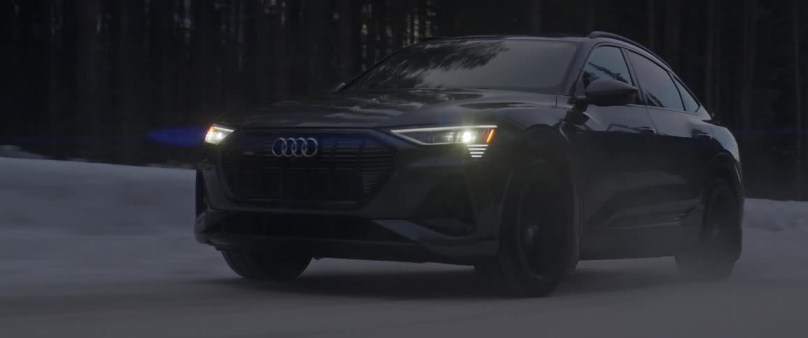 A black audi automobile travels on a snow covered road