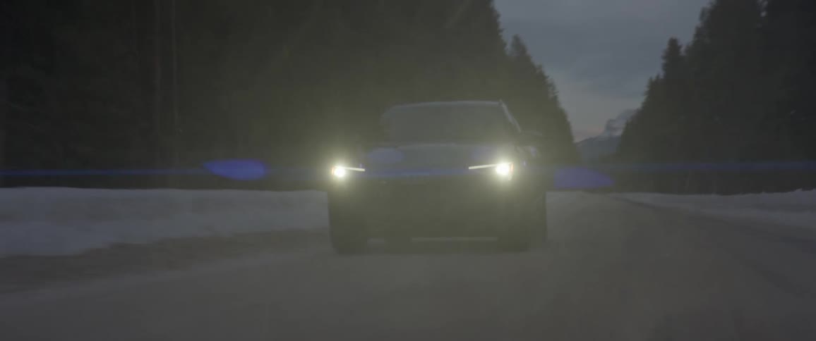 A vehicle driving on a snowy road with trees the sky and clouds in the background