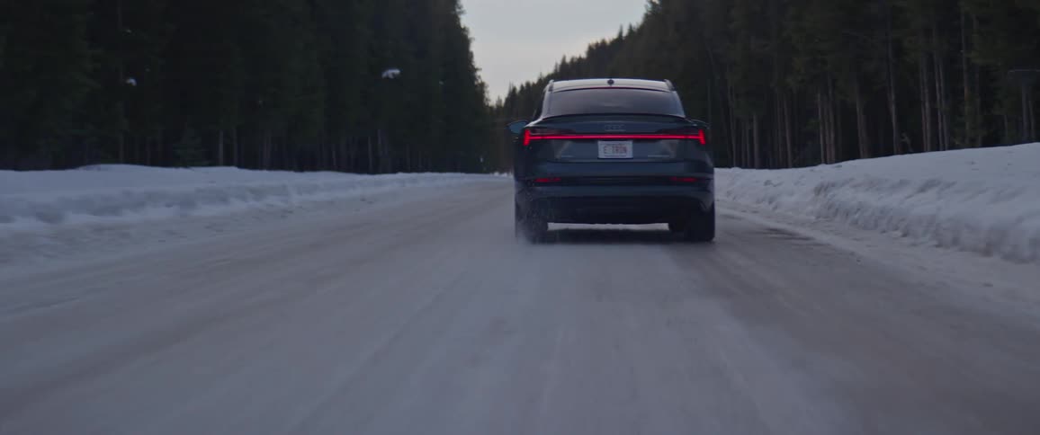 Black car drives along road bordered by snow and conifer forest