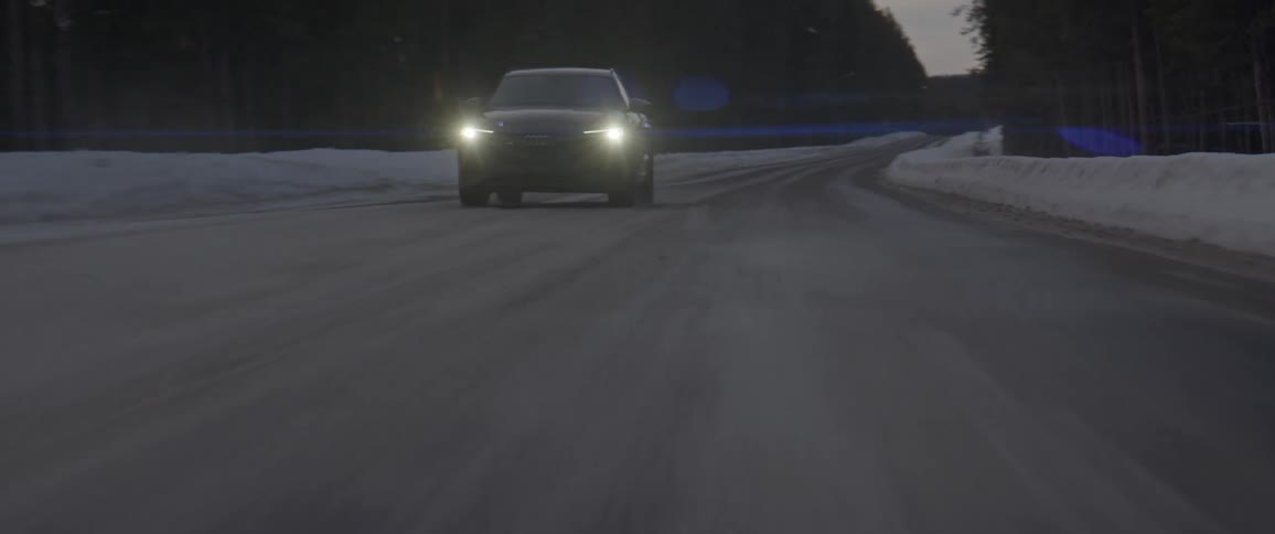 A vehicle with headlights driving on a snowy road with trees in the background