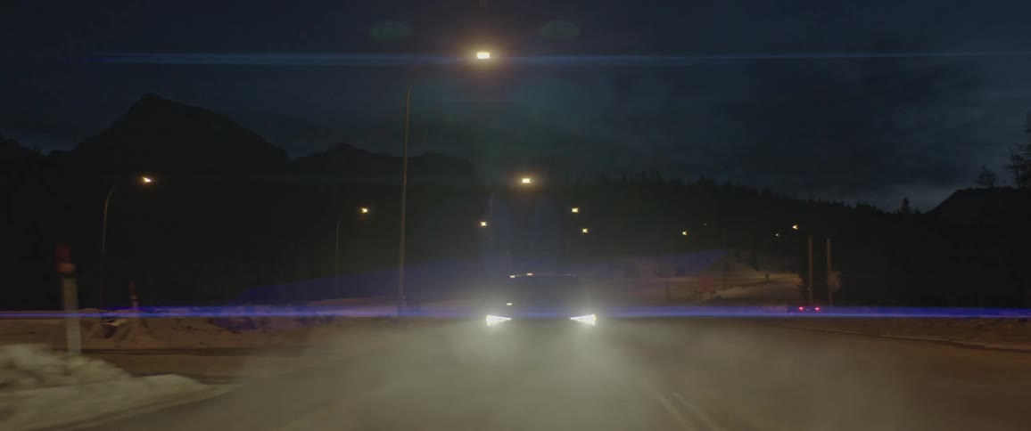 Car with headlights on driving on a road in winter at night
