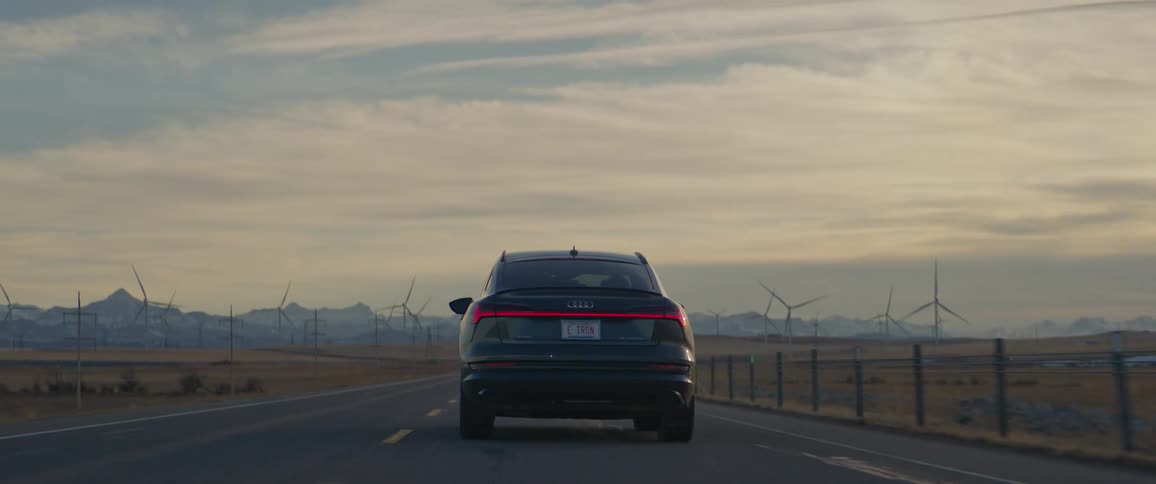 A vehicle drives an open road next to a field of wind turbines