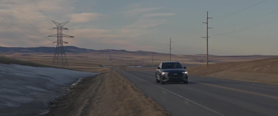 A car is driving on an empty highway at dusk